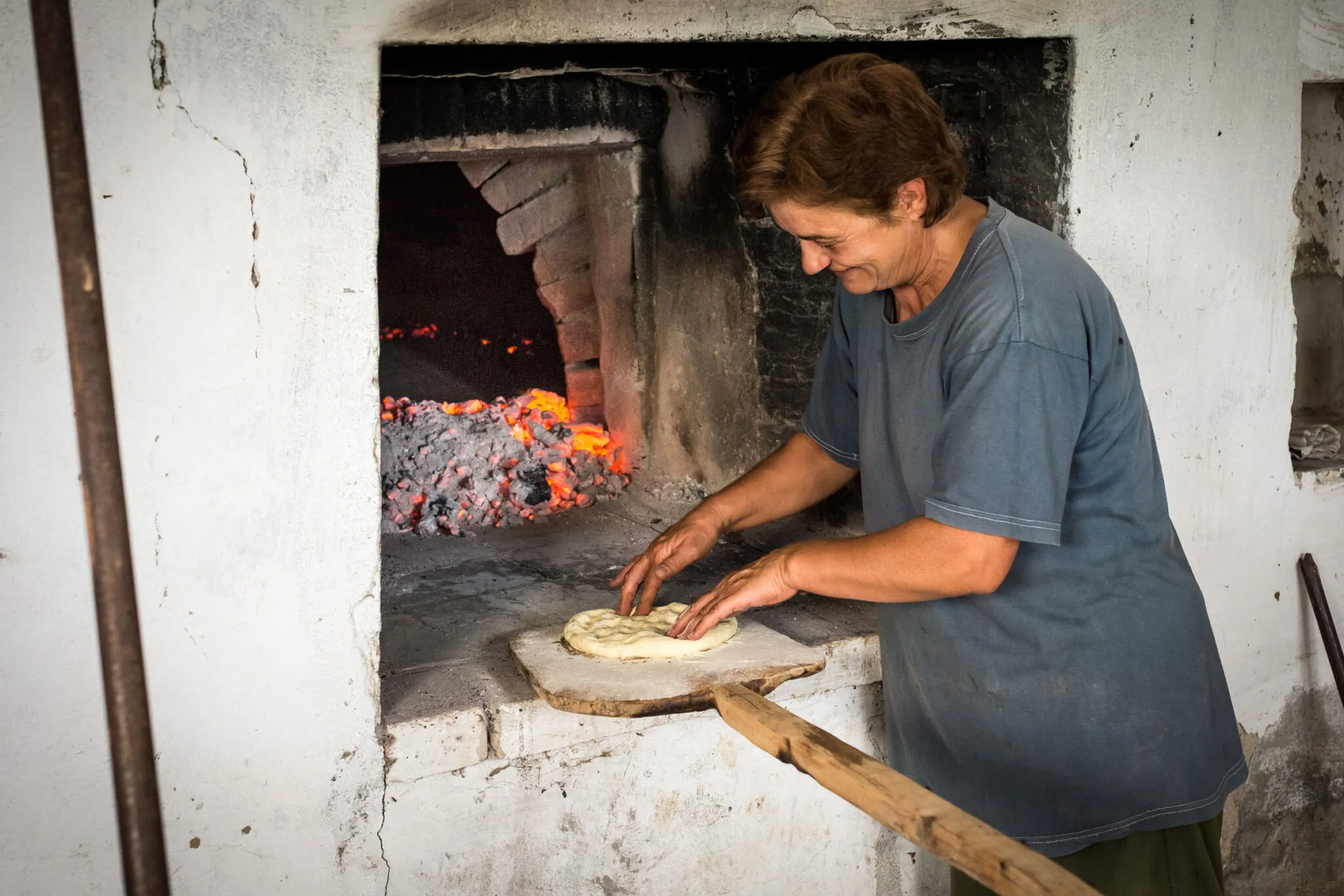 A woman prepares bread next to a wood fired oven