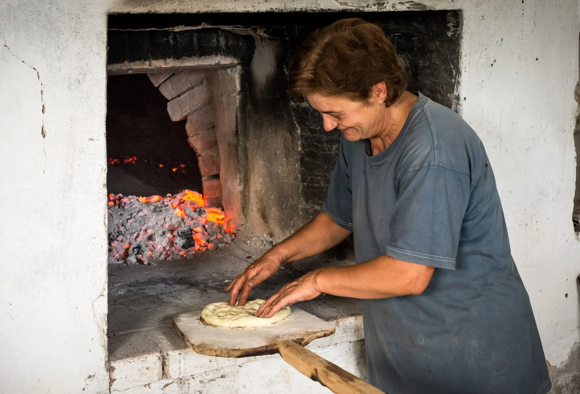 A woman prepares bread next to a wood fired oven