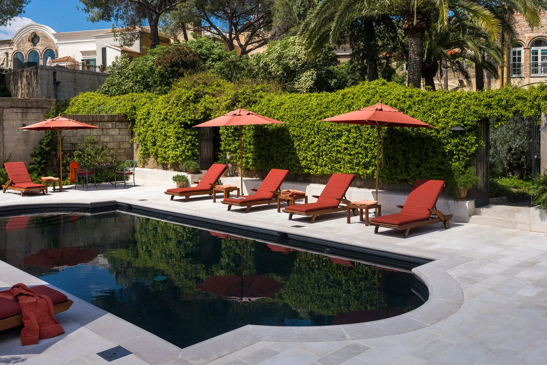 Lounge chairs with red cushions positioned around an outdoor pool