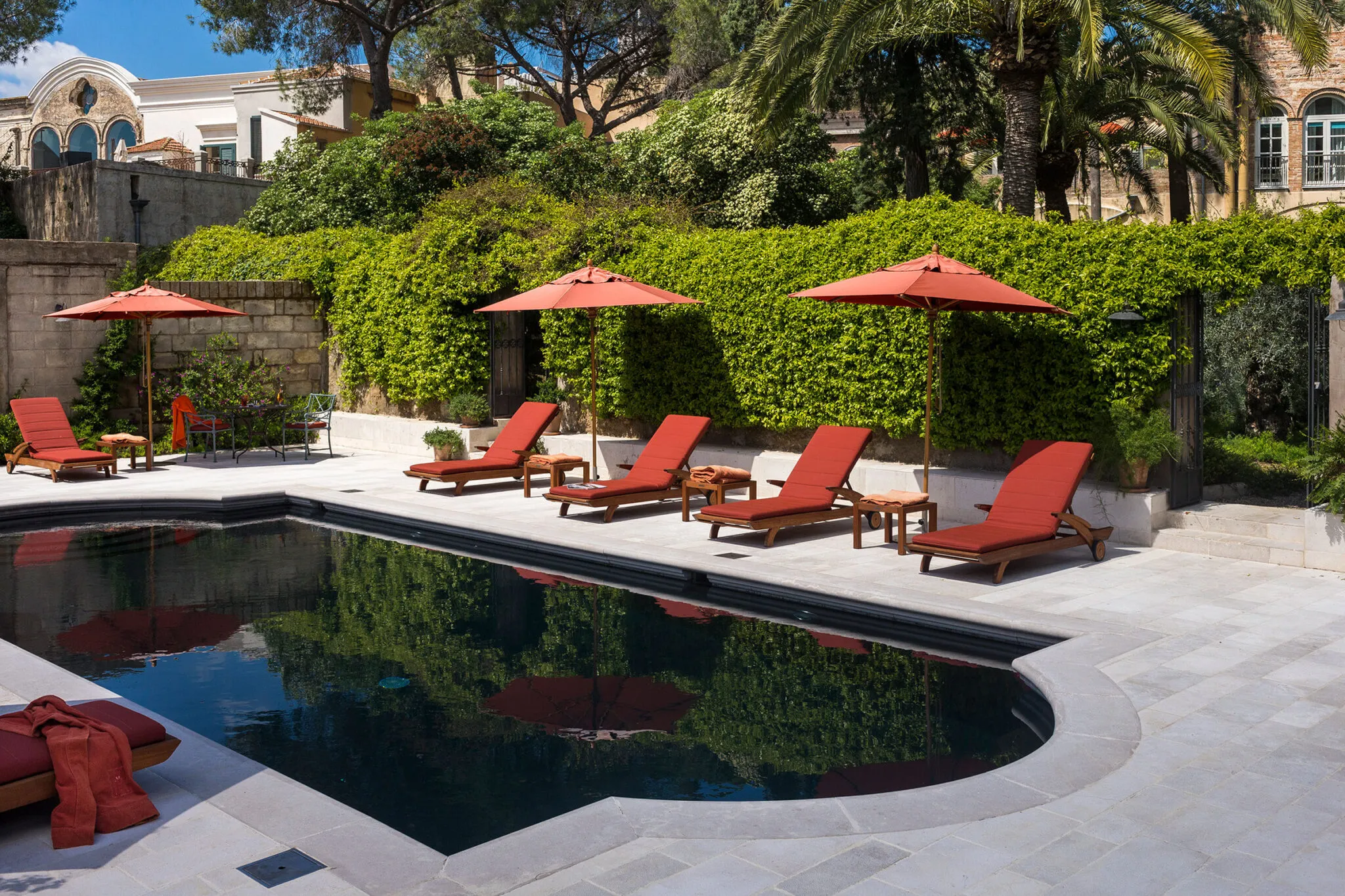 Lounge chairs with red cushions positioned around an outdoor pool