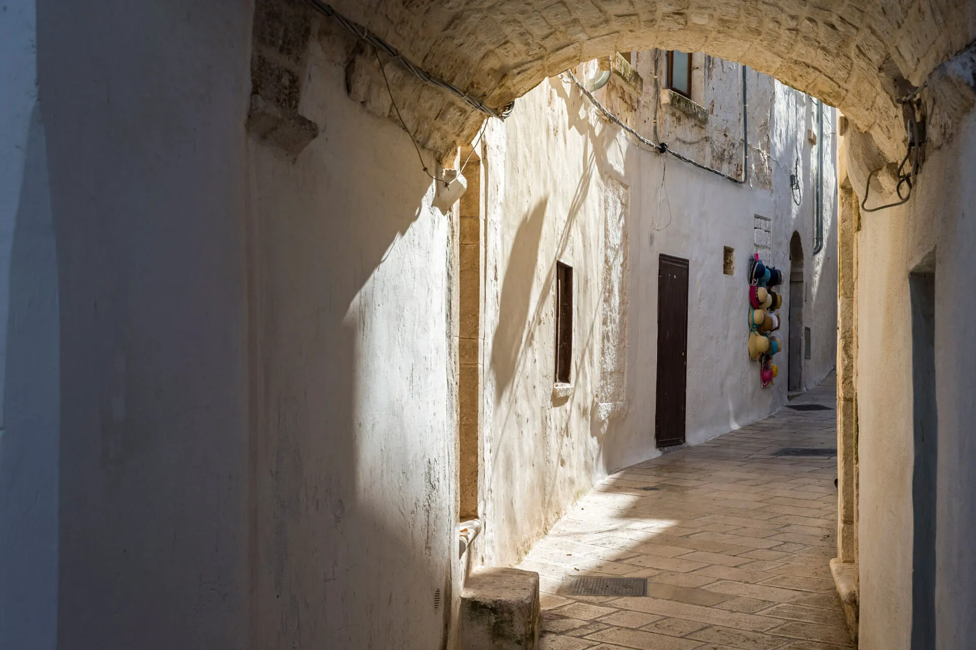 a stone walkway between buildings with a hat shop in the distance